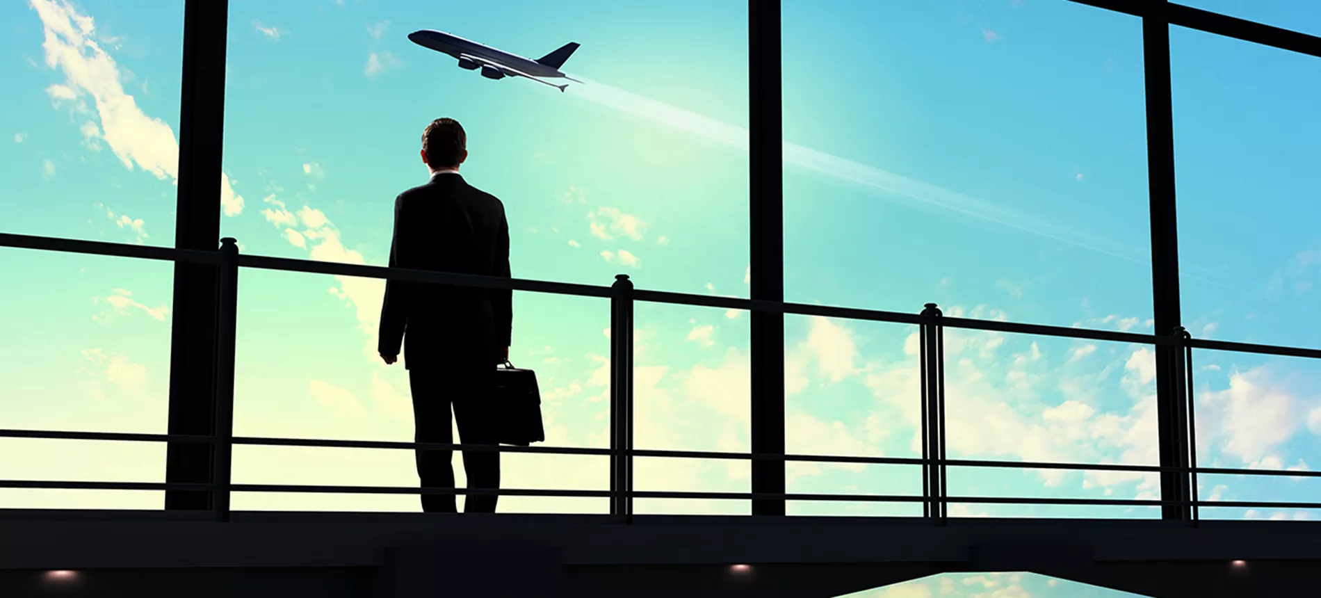Mann i dress og koffert som står og ser ut vinduet på flyplass
