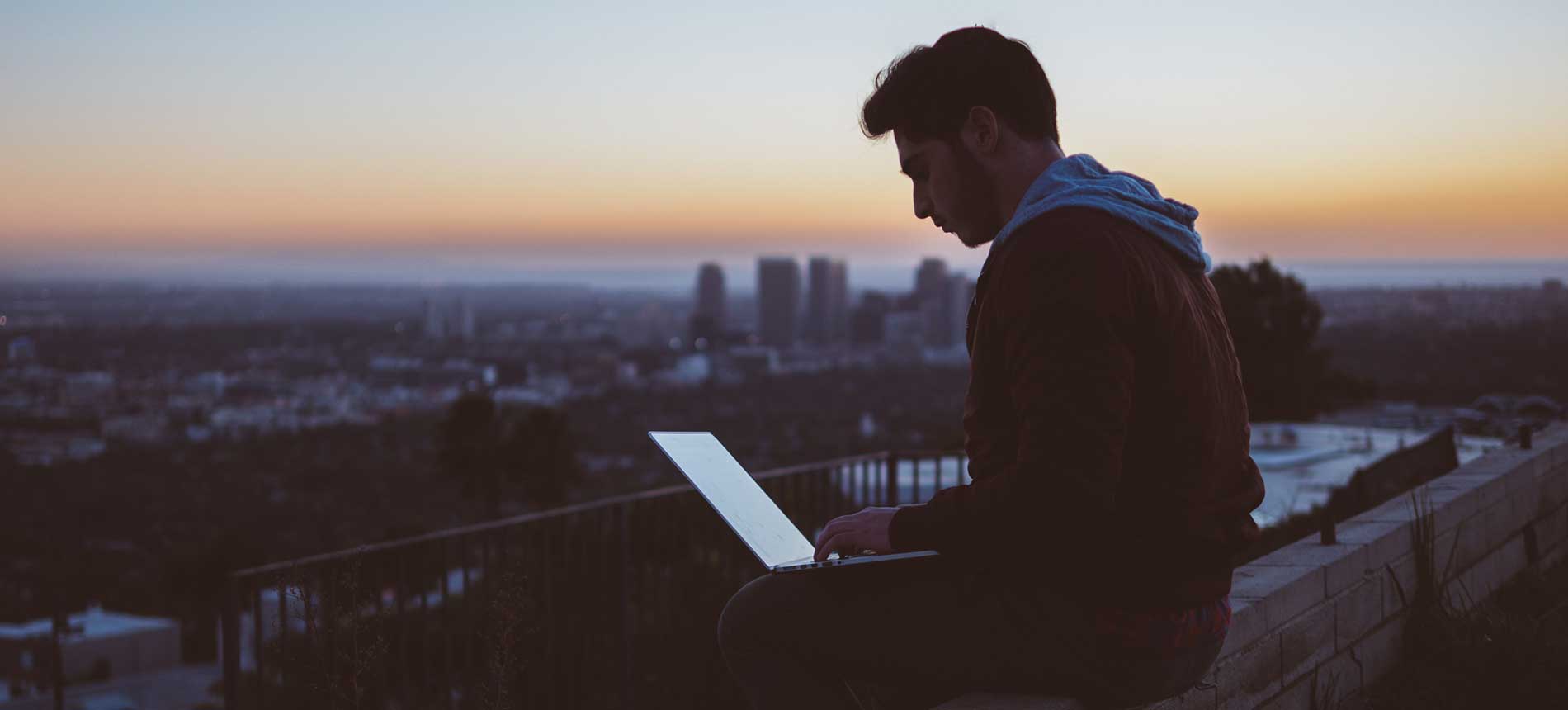 Mann som sitter på taket med PC på fanget i solnedgang