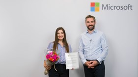 En dame med blomster i hånda og en mann med Microsoft logo bak