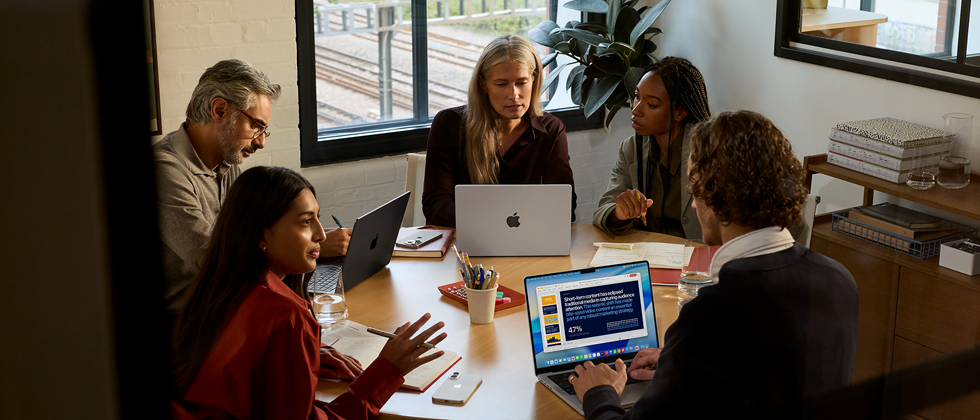 En gruppe med fem ansatte sitter rundt et møtebord og tre MacBook Pro brukes under møtet.