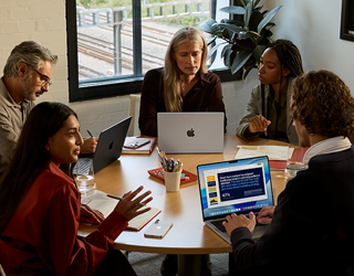 En gruppe med fem ansatte sitter rundt et møtebord og tre MacBook Pro brukes under møtet.