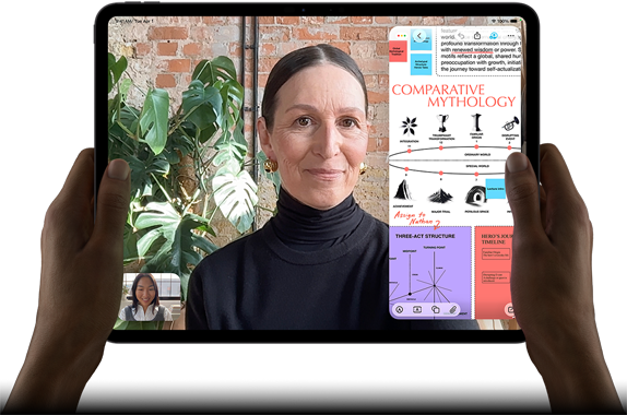 En iPad Pro i fargen stellarsvart vises forfra i liggende retning. Enheten har avrundede hjørner og svart kant rundt skjermen. Den holdes av hender på venstre og høyre side. Skjermen viser en FaceTime-samtale som oversettes direkte, og en lærerik app viser en presentasjon av «Comparative Mythology» med tekst, diagrammer og håndskrevne notater.